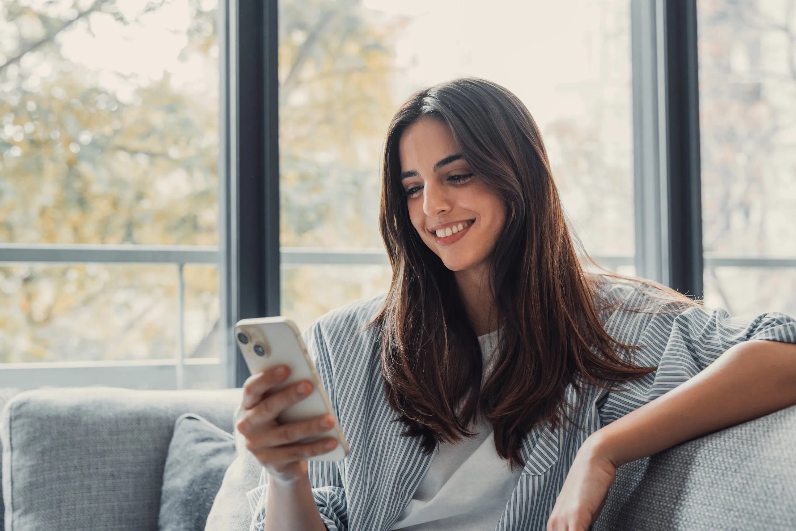 A smiling woman relaxing on her sofa at home, looking at her phone